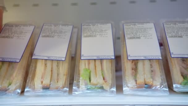Чоловік бере смачні бутерброди з полиці в сучасній супермаркеті. — стокове відео