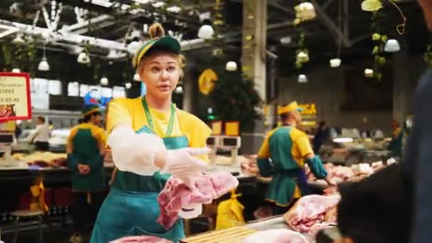 Продавщица показывает мясо свинины клиенту возле прилавка на рынке — стоковое видео