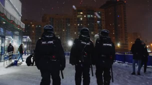 Rendőrök botokkal sétálnak el a stadion mellett télen este. — Stock videók