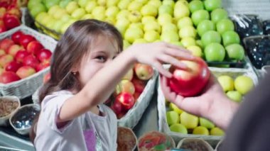 Küçük kız markette babasına lezzetli elmalar veriyor.