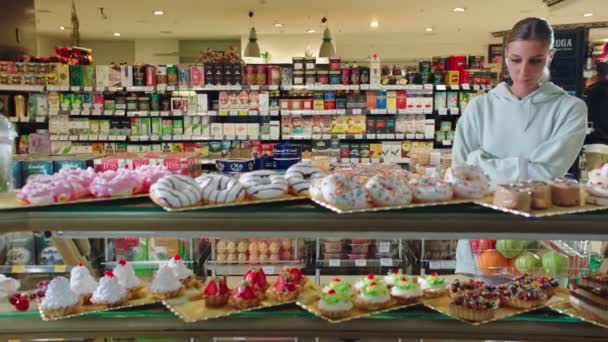 Женщина смотрит на вкусные торты и пончики на витрине магазина — стоковое видео