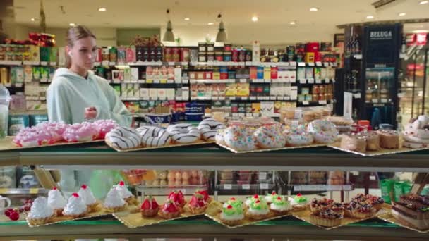 Девушка покупает вкусные пончики с розовой глазурью в супермаркете — стоковое видео