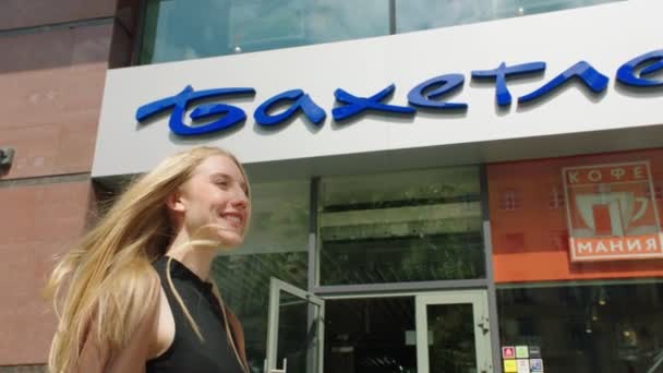 Mujer sonriente pasea por el supermercado y la cafetería en la calle — Vídeo de stock