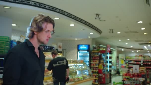 Хлопець у сорочці розмовляє з продавцем у сучасній супермаркеті. — стокове відео