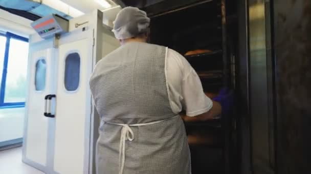 Kvinna tar rack med bröd från ugn i bageriet verkstad — Stockvideo