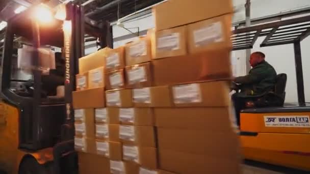 Trabajador lleva cartón en carretilla elevadora a lo largo de almacén — Vídeos de Stock