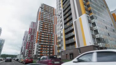 Bulutlu gökyüzünün altındaki konut binalarının önünden geçen yol boyunca hareket