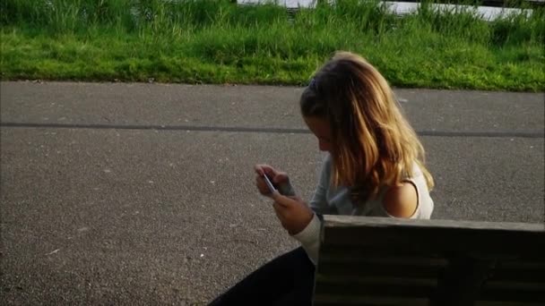 Menina falando no telefone com amigo, menina feliz no parque jogando no smartphone — Vídeo de Stock