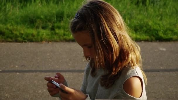 Κορίτσι μιλάει στο τηλέφωνο με φίλο, ευτυχισμένος κορίτσι σε πάρκο που παίζουν σε smartphone — Αρχείο Βίντεο