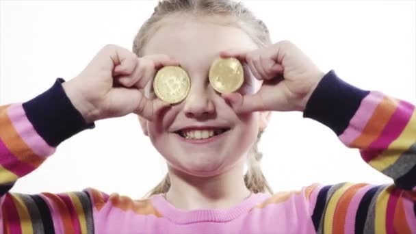 明るい 幸せな女の子彼女の手で黄金の Bitcoin を保持して 白い背景の上のカメラを見て笑みを浮かべて — ストック動画