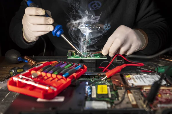 Handen van een man in witte handschoenen reparatie laptop met behulp van soldeerbout — Stockfoto