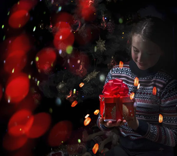 Vrolijk meisje met een geschenk in haar handen op een donkere achtergrond met — Stockfoto