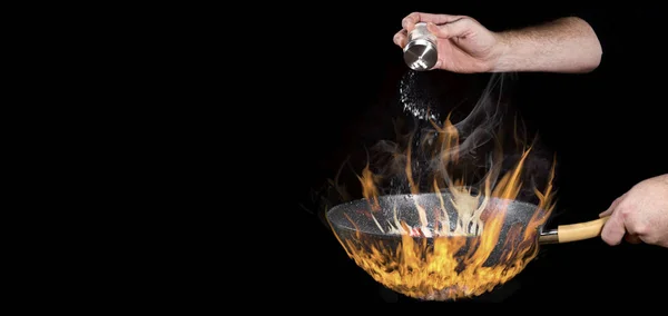 The chef adds salt to the food  over very high heat