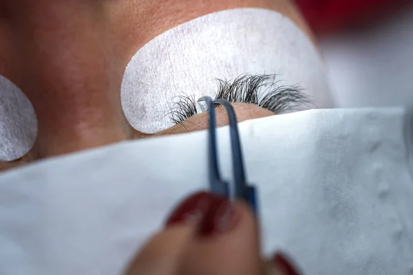 Gluing artificial eyelashes with tweezers. Cosmetic procedure.