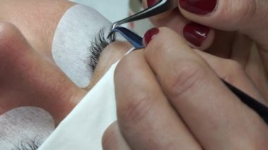 Yapay kirpikleri cımbızla yapıştırmak. Kozmetik prosedürü. Kirpik uzatma. Uzun kirpikli kadın gözü