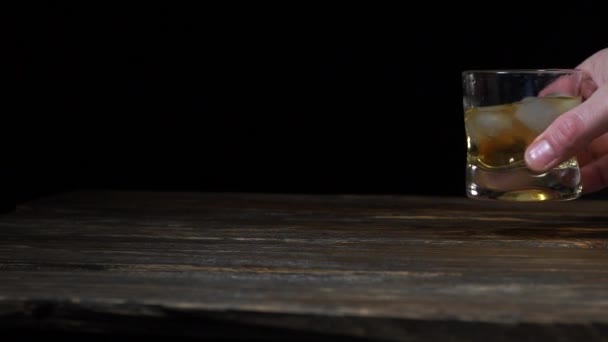 Tenez à la main un verre de whisky avec des glaçons sur le fond noir. Homme secouer le verre de whisky avec des glaçons 