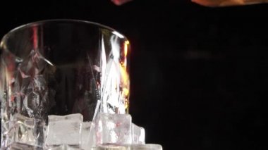 Eski viski bardağa dökülüyor. Koyu arkaplanda buz küpleri olan bardaklara viski ya da konyak dökmek