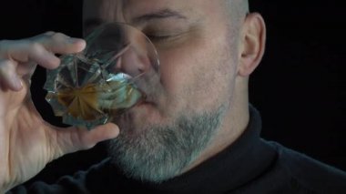 Duygusal sakallı adam buzlu viski içer. Siyah arka planda izole edilmiş, yakın plan portresi. Alkol ve alkol bağımlılığı konsepti. Adam alkolden ürker..