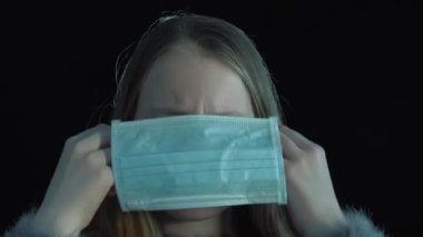 Hasta kız tıbbi maske takıyor. Siyah arka planda tıbbi maskeli hasta bir kızın portresi.