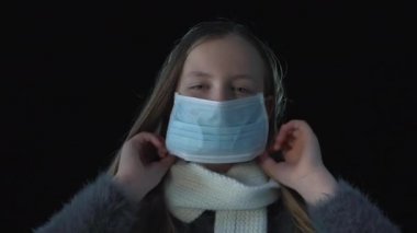 Hasta kız tıbbi maske takıyor. Siyah arka planda tıbbi maskeli hasta bir kızın portresi. Öksür. Koronavirüs konsepti