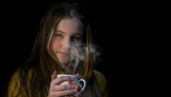 The girl is warming with hot drink. Girl holds a mug of hot tea in her hand