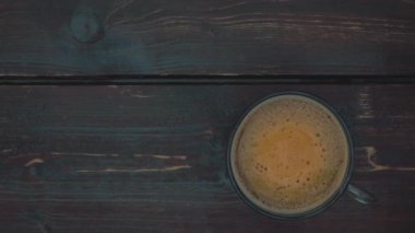 Kahve köpüklü cam bardak ve kahve. Masanın eski püskü koyu kahverengi yüzeyi. Üst alt görünüm.