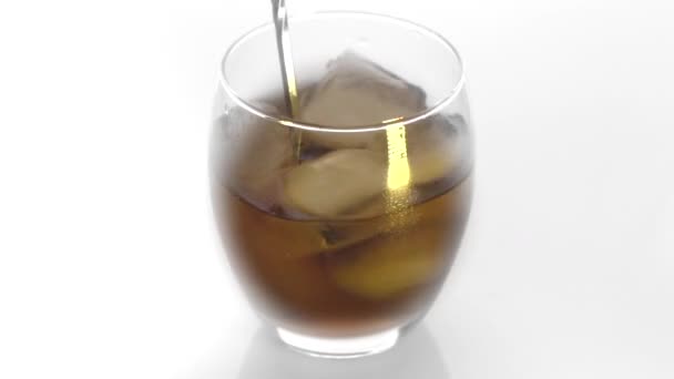 接近中だ 氷のキューブが回転し ウイスキーのガラスに溶けます 白い背景に隔離されている 白い背景にウイスキーのアイスバスを回転させる — ストック動画