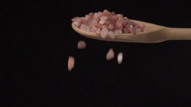  Pembe Himalaya tuzu, siyah bir arka planda tepeden tırnağa ahşap bir kaşıktan yavaş çekimde akıyor..