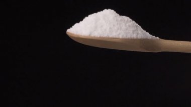 Tuz, siyah arka planda tepeden tırnağa ahşap bir kaşıktan dökülüyor..