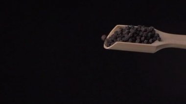 Kara biberler, siyah arka planda ağır çekimde tepeden tırnağa ahşap bir kepçeden dökülür..