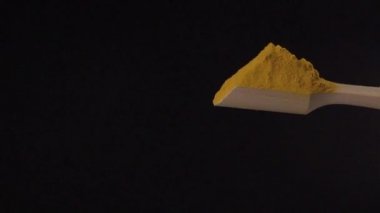 Curcuma tozu, siyah arka planda yavaş çekimde tepeden tırnağa ahşap bir kepçeden dökülür.