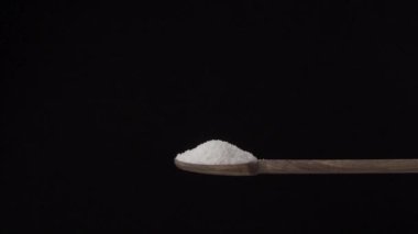 Siyah bir arka planda ağır çekimde ahşap kaşıktan dibe tuz dökülüyor. 