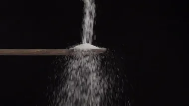 Siyah bir arka planda ağır çekimde ahşap kaşıktan dibe tuz dökülüyor. 