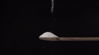 Siyah bir arka planda ağır çekimde ahşap kaşıktan dibe tuz dökülüyor. 