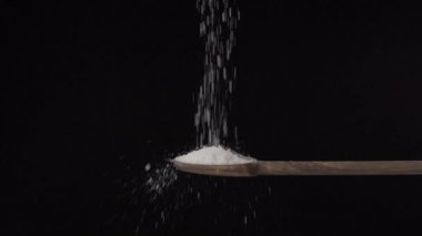 Siyah bir arka planda ağır çekimde ahşap kaşıktan dibe tuz dökülüyor. 