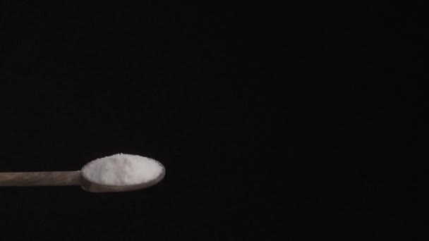 黒の背景にゆっくりとした動きで木製のスプーンから底に塩を注ぐ — ストック動画