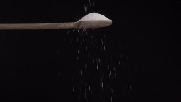 在黑色的背景上缓慢地从木勺往下倒盐 — 图库视频影像