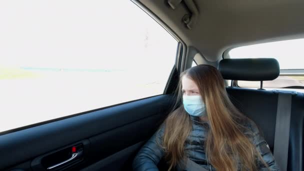 一个戴口罩的疲倦的女孩坐在汽车后座上 望着车窗 — 图库视频影像