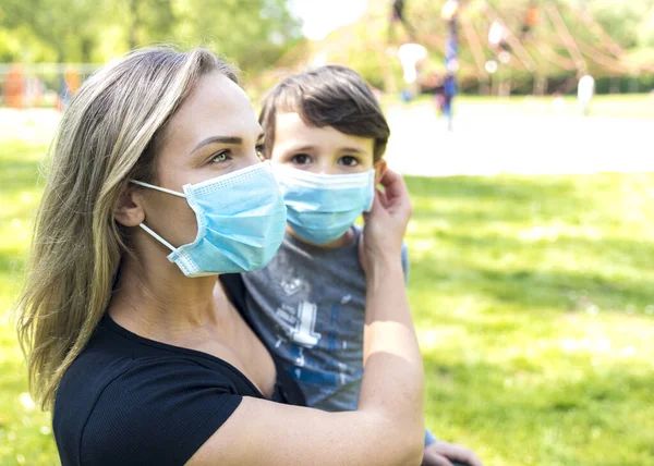 Anne ve oğlu çocuk parkında maskeli. İnsanlar salgın veya grip salgını sırasında koruyucu bir tıbbi maske takarlar. Kişisel koruma ekipmanları. Anne bebeğine antiseptik veriyor.