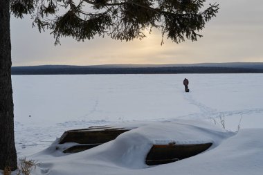 Şafak vakti karla kaplı göl ve kıyıda tekneler. Dağlarda karla kaplı köknar ağaçları olan kış ormanı..