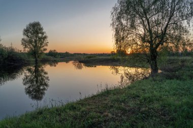 Gölün üstünde şafak. Gün batımında parlayan parlak ışık bulutlarıyla güzel bir akşam masmavi gökyüzü. Sıcak yaz akşamı gün batımında.
