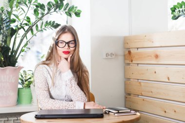 Gözlüklü, iş yerinde oturan gülümseyen genç bir iş kadınının portresi.