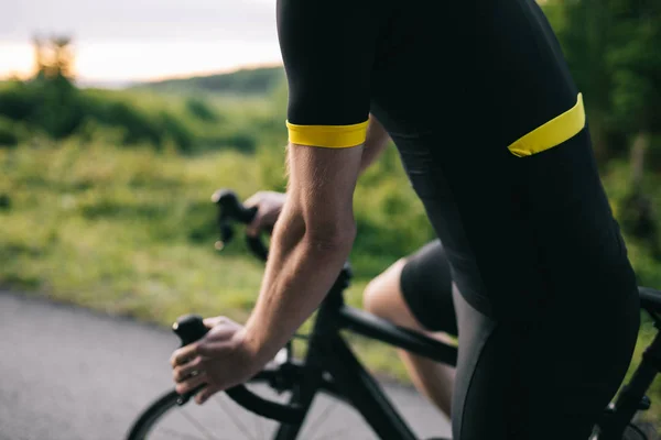 Ormandaki yolda siyah formalı bir bisikletçi.