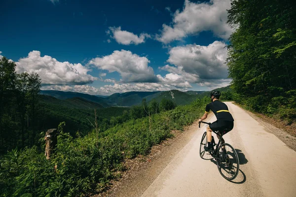 Ormandaki yolda siyah formalı bir bisikletçi.