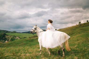 Gelinlikli gelin beyaz bir ata biniyor.