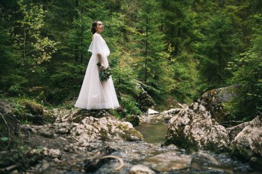 Doğada poz veren beyaz elbiseli güzel gelin