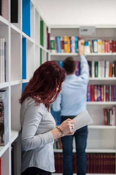 Gyönyörű vörös hajú diák lány gazdaság könyv a könyvtárban — Stock Fotó