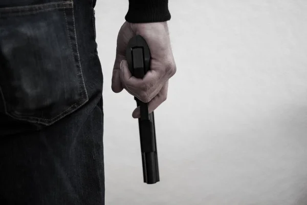 Killer håller en pistol till hans fötter, vit bakgrund framför h — Stockfoto