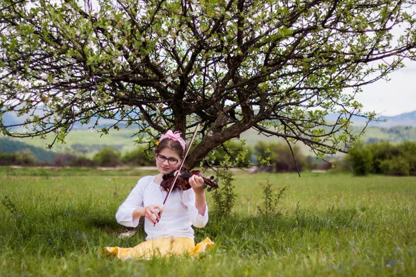 Menina loira bonita sentada em uma bela grama verde cheia de — Fotografia de Stock
