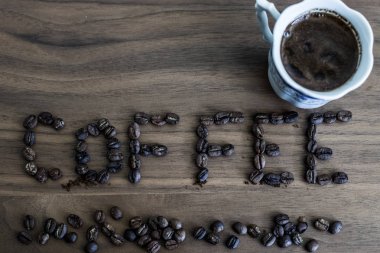 Kavrulmuş kahve çekirdekleri, masanın üzerine dağılmış ve kahve yazılı,